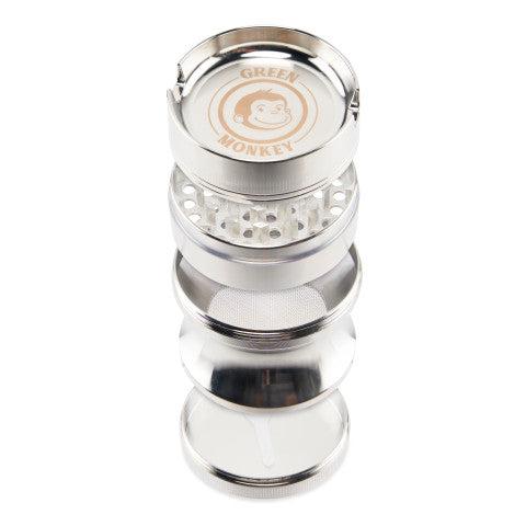 Top-down view of a disassembled stack of the Green Monkey Chacma Grinder with Ashtray showing its metallic chambers, teeth, mesh screen, and branded lid.