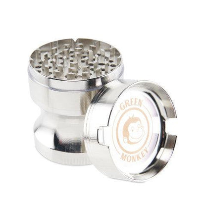 Angled studio shot of the Green Monkey Chacma Grinder with Ashtray in polished silver, lid off to show its toothy grinding chamber and branded cap.